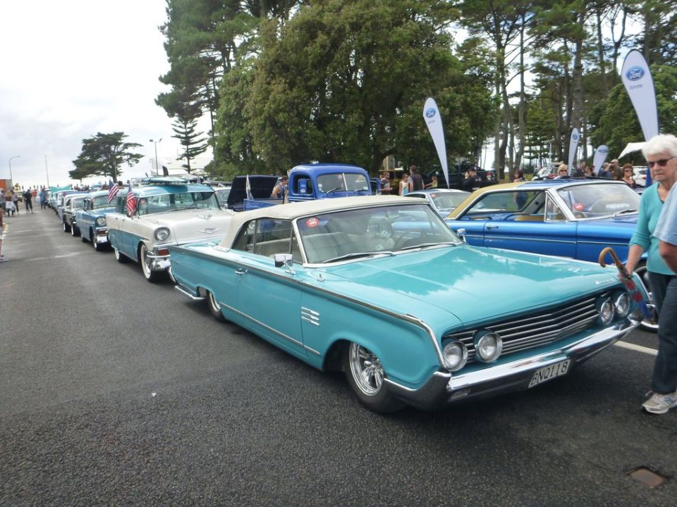 Turquoise convertible with chrome grille and side trim, parked in a line of cars