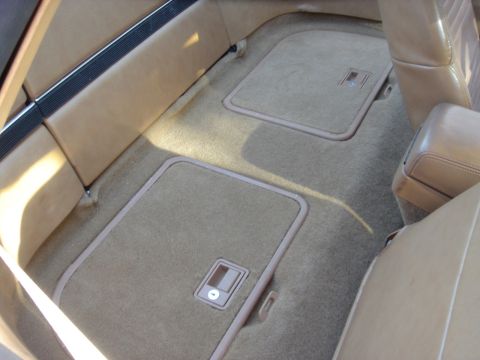 1991 Buick Reatta - The tan carpeted interior of a car shows two floor storage compartments with latches.