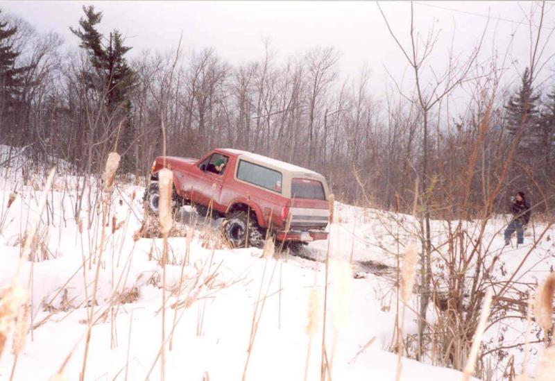 Red SUV with white top climbing through snow off-road, rear 3/4 view