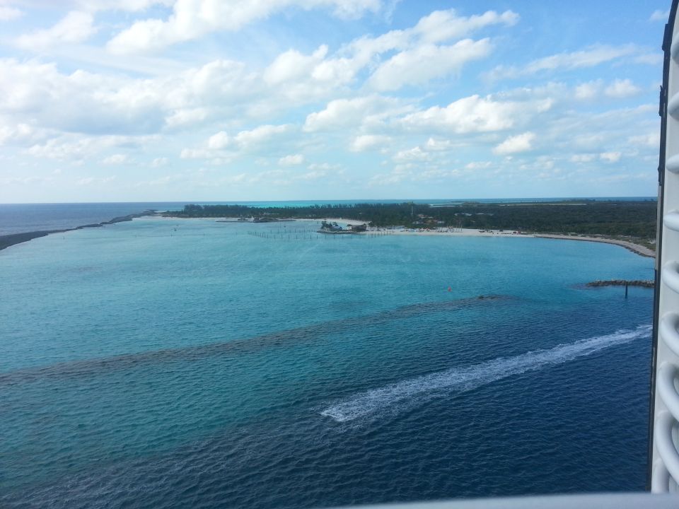 Tropical coastline with turquoise water, a distant island, and a boat wake. Part of a white structure is visible on the right