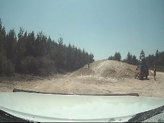 1994 Ford Bronco - A red SUV is parked on a dirt mound in a wooded area under a clear sky.