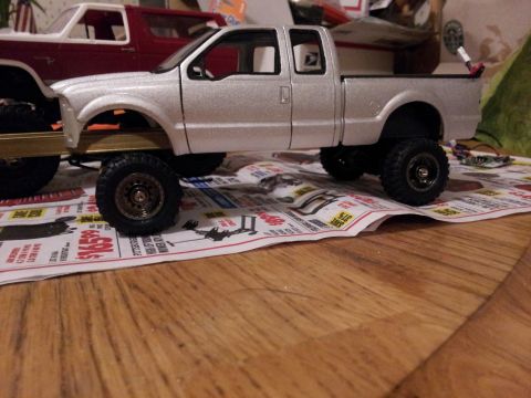 1995 Ford Bronco - A silver model pickup truck sits on a newspaper next to a red model SUV.