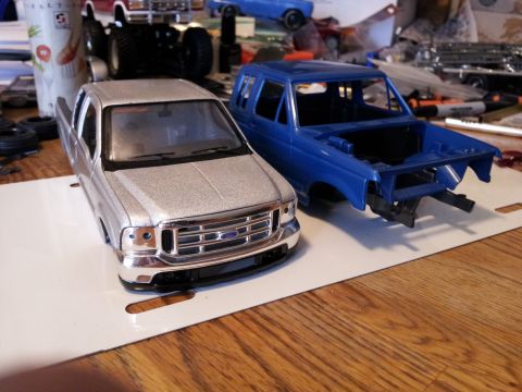 1995 Ford Bronco - Two model vehicle bodies, a pickup and an SUV, sit on a wooden surface with other hobby supplies.