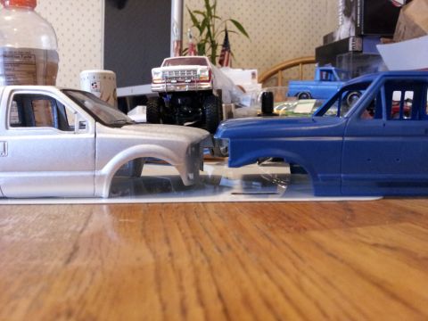 1995 Ford Bronco - Unfinished model truck bodies are displayed on a table, with a partially visible bottle and other items in the background.
