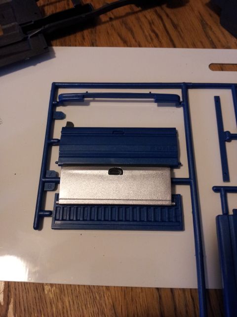 1995 Ford Bronco - Model kit parts for a truck bed, including a silver tailgate, are laid out on a white surface.