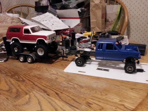 1995 Ford Bronco - Two model vehicles, a Bronco on a trailer and a truck chassis, are displayed on a wooden surface.