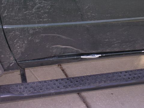 1985 Ford Bronco - The lower body panel of a vehicle shows significant damage, including a large dent and numerous scratches.