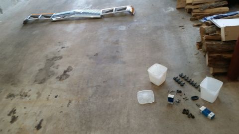 1991 Ford LTD Crown Victoria - A chrome grille and bumper assembly lies on a concrete floor next to various small parts and plastic containers.