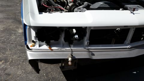 1991 Ford LTD Crown Victoria - The front end of a white vehicle is shown with its hood open and lights removed for repair.