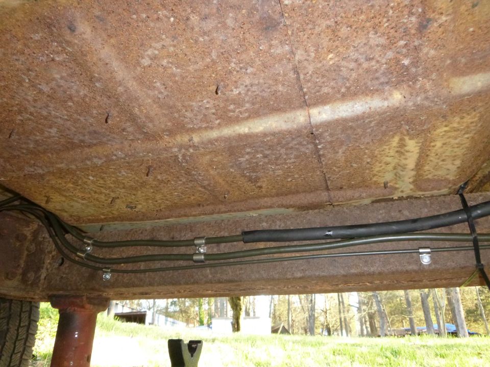 Underside of a rusty vehicle frame with brake lines and hoses attached