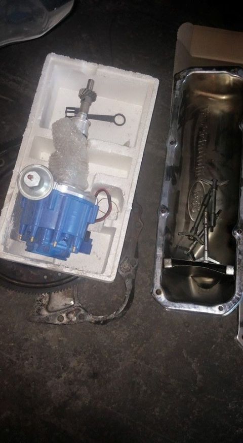 1979 Ford Bronco - Engine parts, including a blue distributor and an oil pan, are laid out on a dark surface.