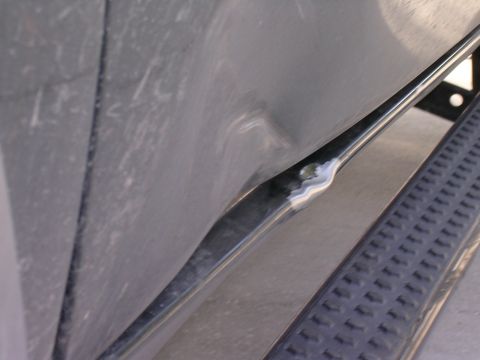 1985 Ford Bronco - Close-up view of a dented metal trim piece and a textured step on a vehicle.
