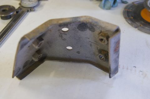 1979 Ford Bronco - A metal bracket with visible rust and bolt hardware sits on a workbench next to tools.