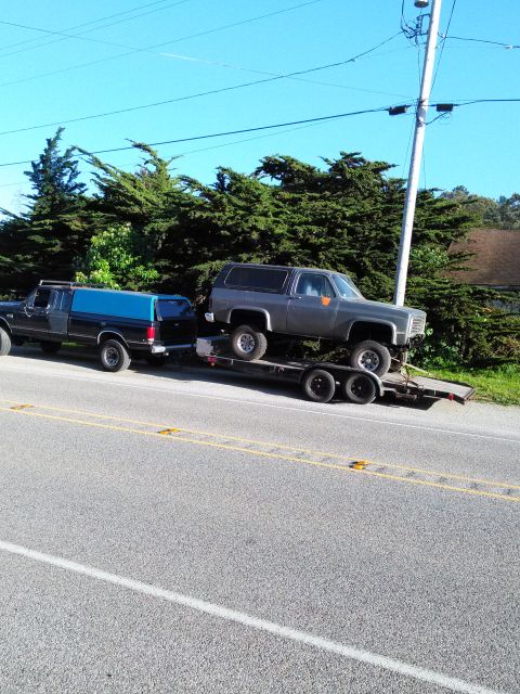 1991 Ford Bronco - A gray SUV, likely from 1973 based on its body style, is transported on a trailer towed by a pickup truck.