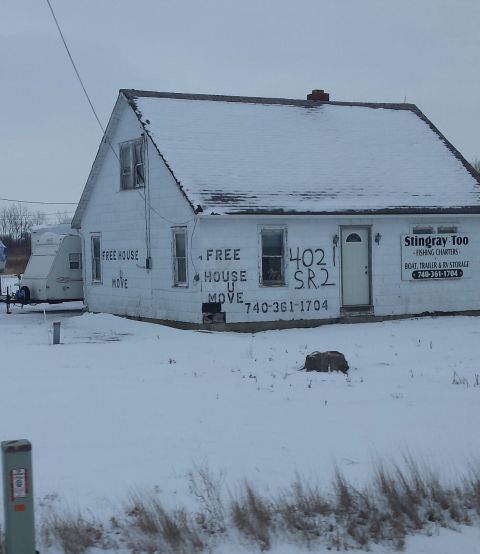 1995 Ford Bronco - A house covered in snow features graffiti and a business name, with a trailer parked nearby.