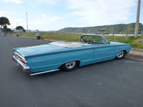 1964 Mercury Monterey - A classic blue convertible with a white top sits parked by the ocean on a cloudy day.