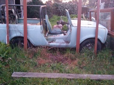 1991 Ford Bronco - An abandoned light blue SUV sits in tall grass, missing its doors and roof.