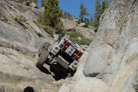 1961 International Scout 800 - An off-road vehicle navigates a steep, rocky terrain under a clear blue sky.