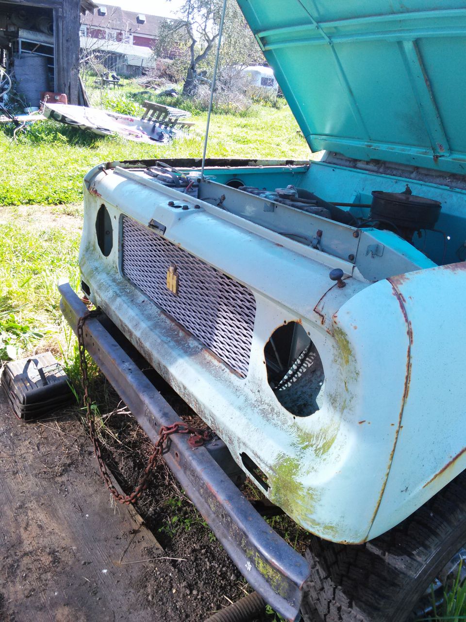 Light blue International Harvester Scout with hood open, showing a rusty bumper and grille
