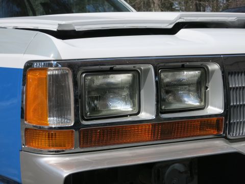 1991 Ford LTD Crown Victoria - Close-up of a white and blue vehicle's front end, showing its headlights and grille.