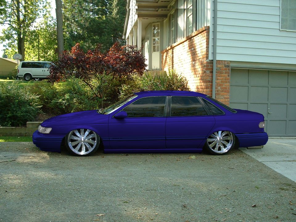 Purple Ford Taurus sedan lowered onto chrome wheels, side view in a driveway