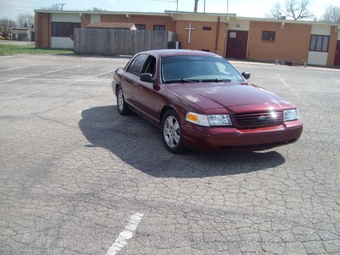 2004 Ford Crown Victoria - A maroon sedan is parked in an empty lot with a building behind it.