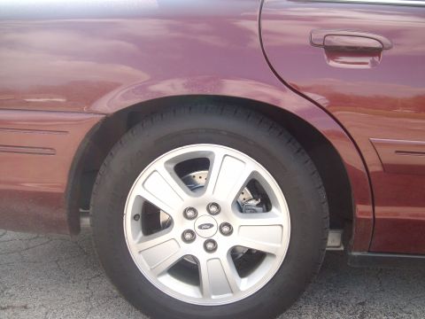 2004 Ford Crown Victoria - The rear wheel and fender of a maroon sedan, likely a 2004 Ford Crown Victoria, are visible.