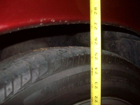 2004 Ford Crown Victoria - A yellow measuring tape is placed in the wheel well of a red vehicle, indicating a height measurement.