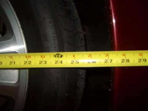 2004 Ford Crown Victoria - A tape measure is used to show the distance between the tire and the fender, indicating a measurement of approximately 25 inches.