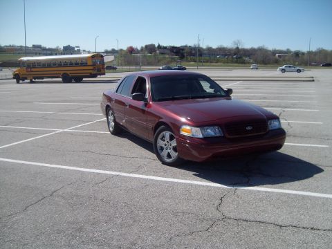 2004 Ford Crown Victoria - A maroon sedan is parked in a lot with a school bus visible in the distance.