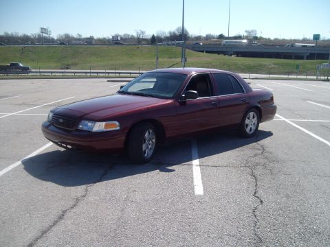 2004 Ford Crown Victoria - A maroon sedan is parked in an empty lot under a clear sky.