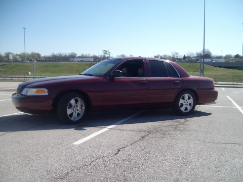 2004 Ford Crown Victoria - A maroon sedan is parked in a lot under a clear blue sky.
