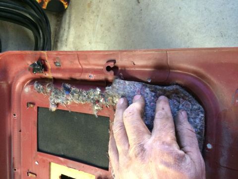 1986 Ford Bronco - A hand is shown removing insulation from the interior of a red car door panel.