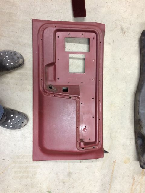 1986 Ford Bronco - A disassembled red car door panel is shown on a concrete floor, with a portion of another car part visible to the right.