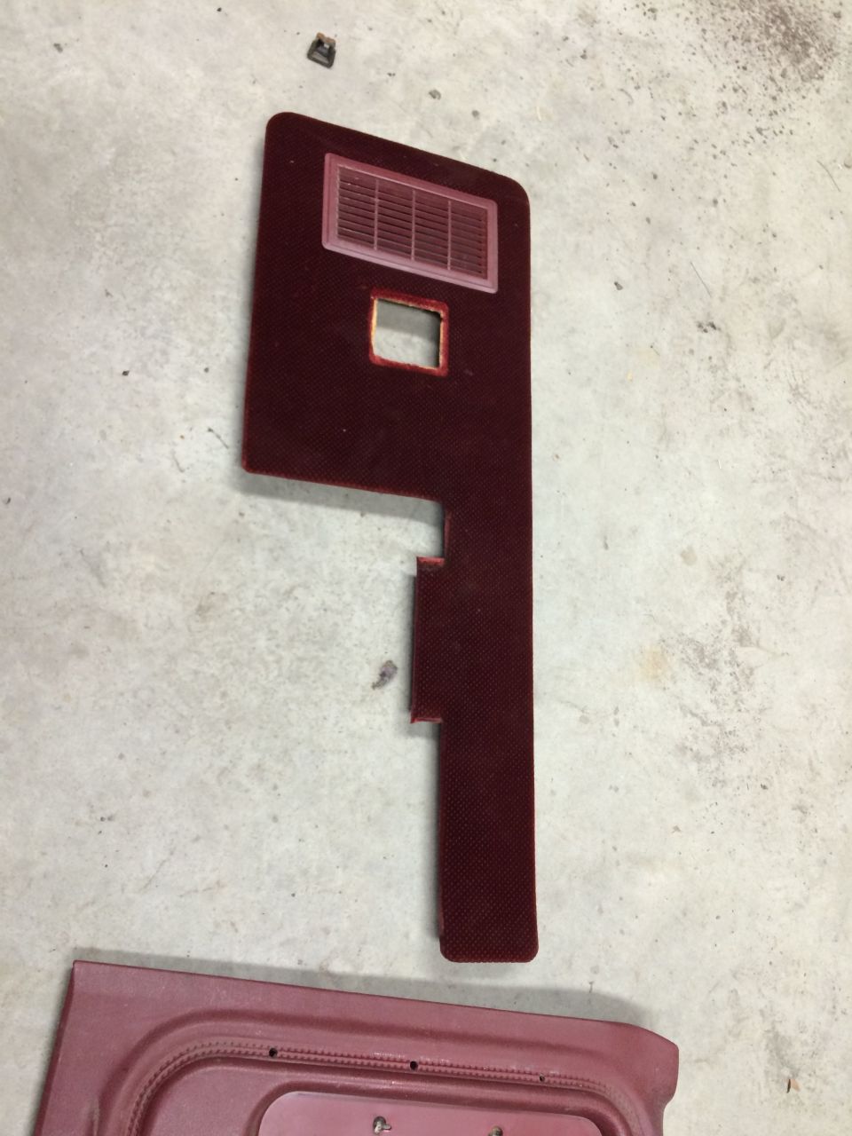 Maroon car door panel with a vent and a square cutout, lying on a concrete floor