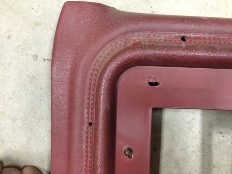 1986 Ford Bronco - This red interior trim piece shows wear and has several screw holes, indicating it's a part removed from a vehicle.