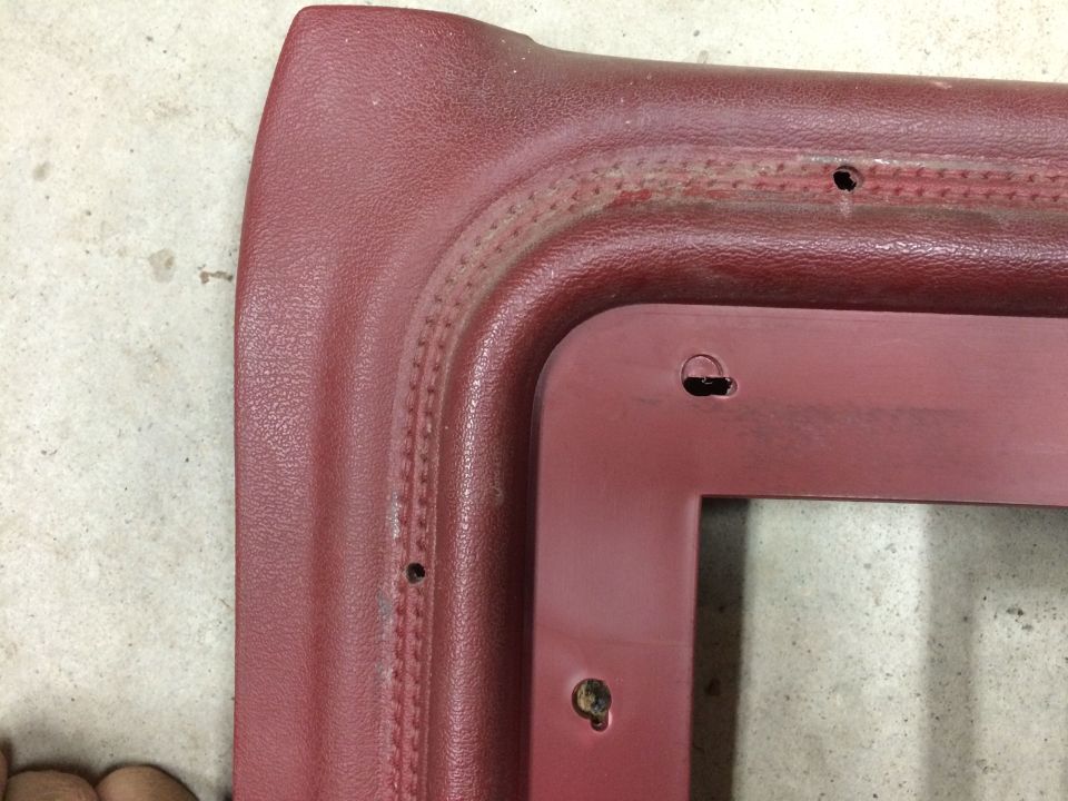 Close-up of a red vinyl interior trim piece with stitched detailing and screw holes