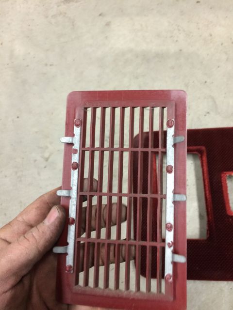 1986 Ford Bronco - A red vent grille with metal clips is held in a hand, with another similar part visible in the background.