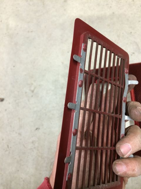 1986 Ford Bronco - A red vent grille with metal bars is held by a hand, showing part of a SuperMotors.net watermark.
