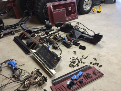 1986 Ford Bronco - Various disassembled parts from a vehicle's interior are laid out on the floor, likely for repair or restoration.