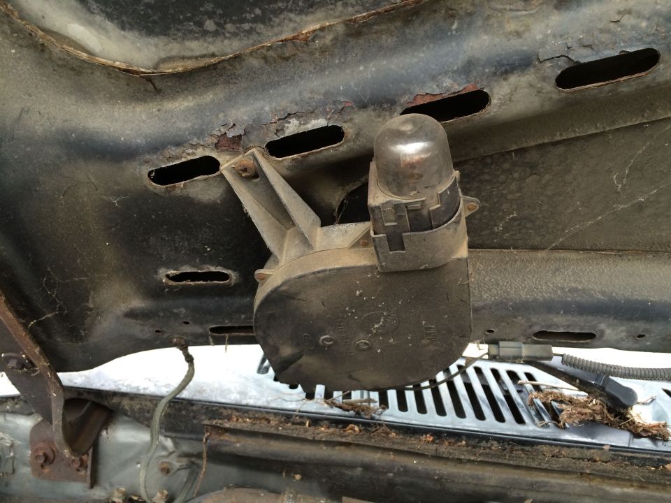 under hood component with a silver dome and black housing, mounted to rusty metal