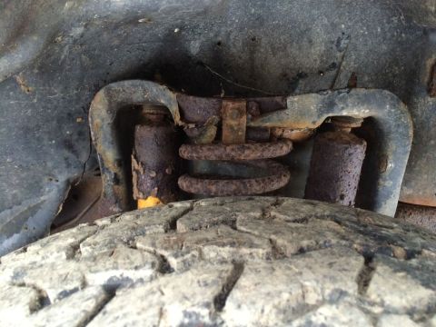 1986 Ford Bronco - Close-up view of heavily corroded suspension parts and a tire, suggesting a vehicle in poor condition.