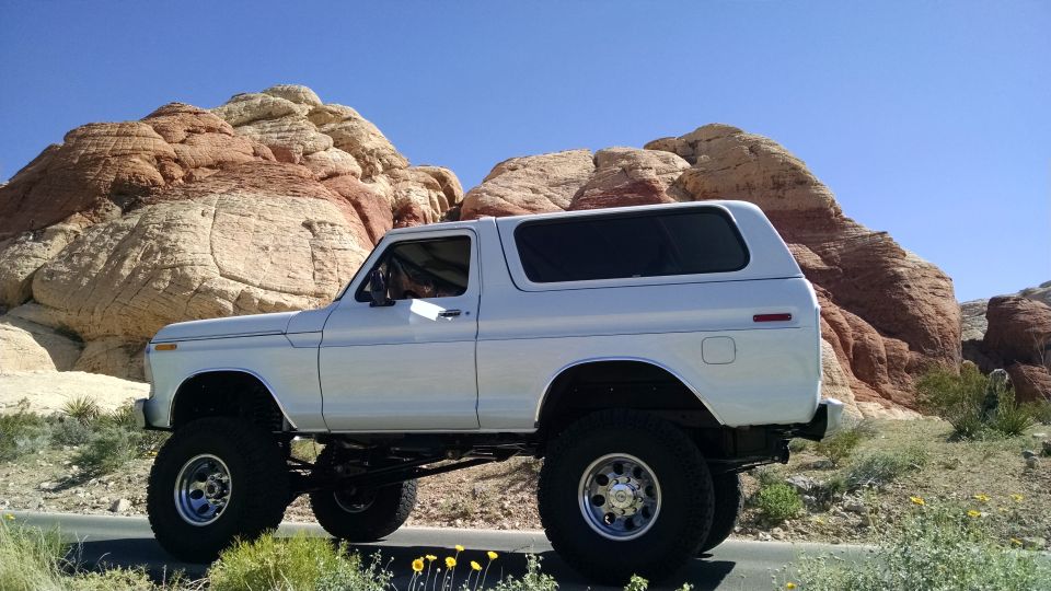 White 1979 Ford Bronco with lifted suspension parked on a road with red rock formations