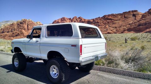 1979 Ford Bronco - This lifted white Ford Bronco is shown from the rear in a desert landscape with red rock mountains.