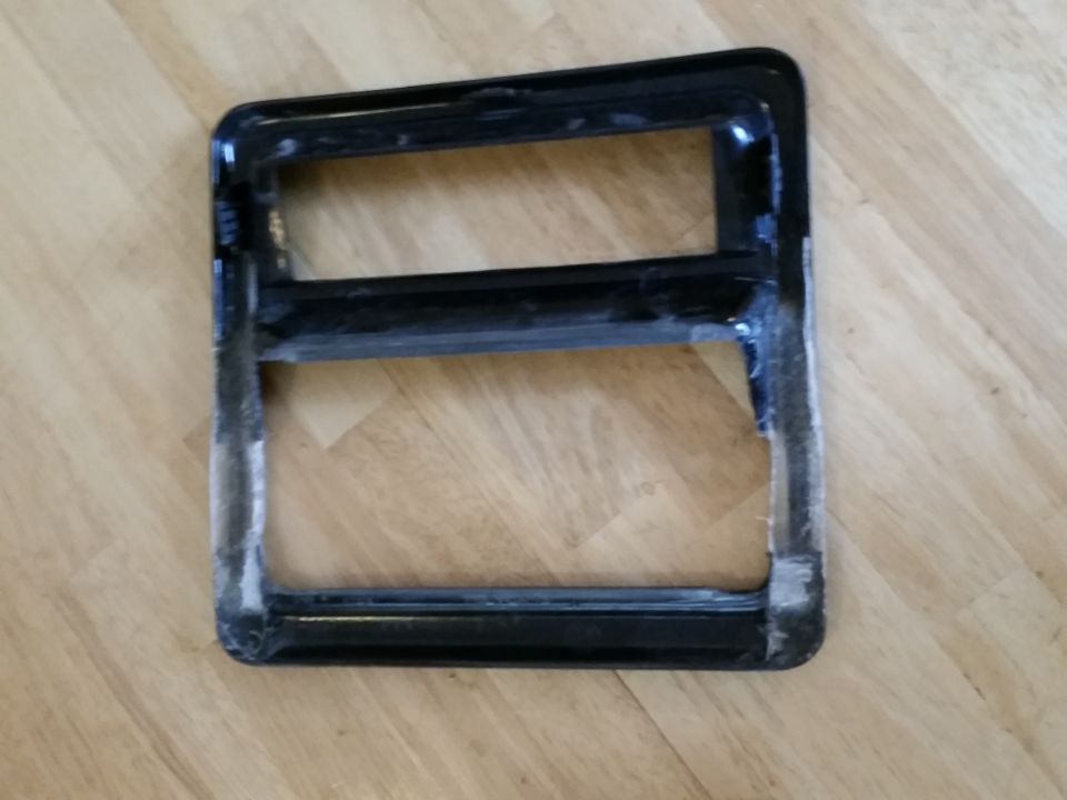 Black plastic trim piece with two rectangular openings, sitting on a wood floor. Supermotors.net logo visible