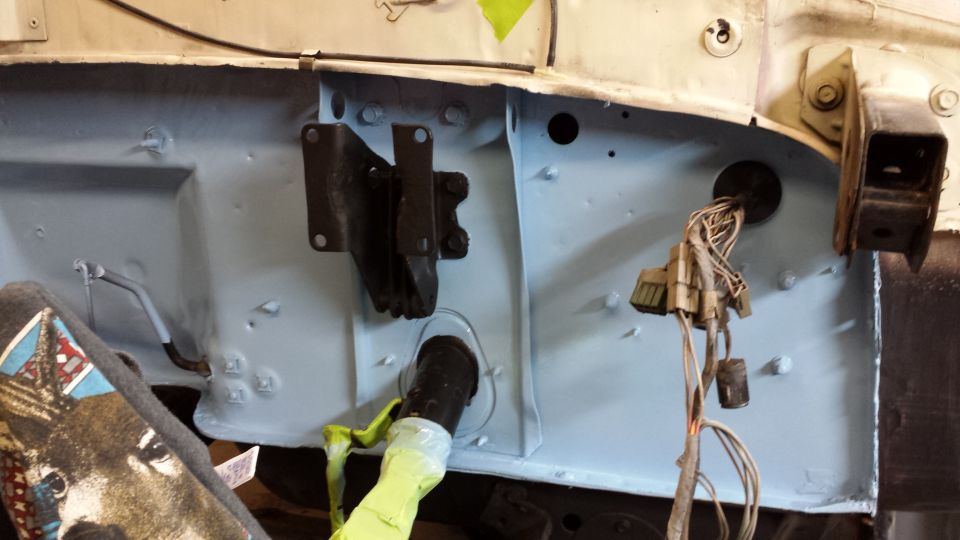 Close-up of a vehicle's firewall with exposed wiring and a black bracket. A black hose with yellow tape is visible