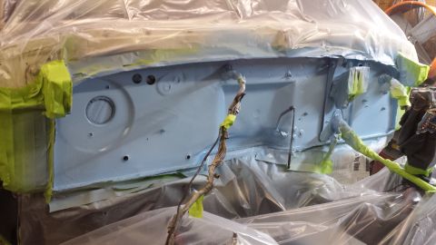 1978 Ford Bronco - The firewall of a vehicle is being prepared for painting, covered in primer and protective sheeting.