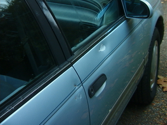 Silver sedan door and front fender showing scattered paint chips and a body-color handle