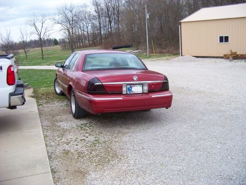 1999 Mercury Grand Marquis - Rear view of a red Mercury Grand Marquis sedan parked on a gravel lot next to a white truck.