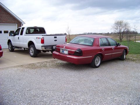 1999 Mercury Grand Marquis - A red 1999 Mercury Grand Marquis is parked in a driveway next to a white pickup truck.